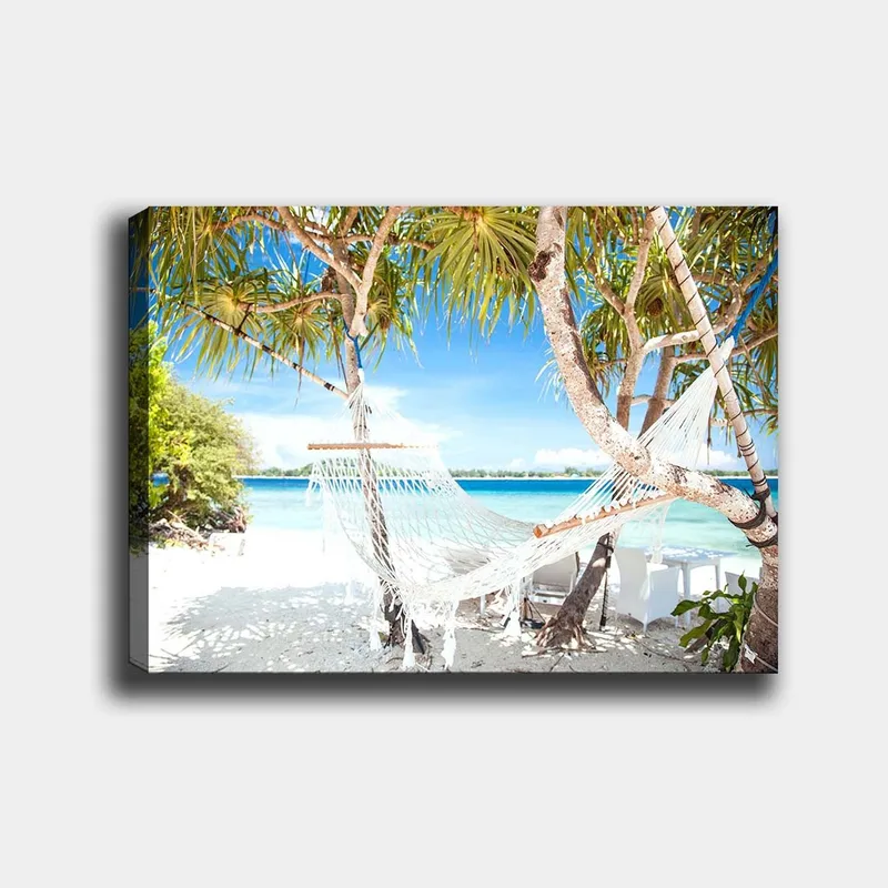 Canvastavla 70x100 cm - Avkopplande hängmatta mellan palmer vid en strand med turkost vatten och klarblå himmel, Vit / Blå / Grön
