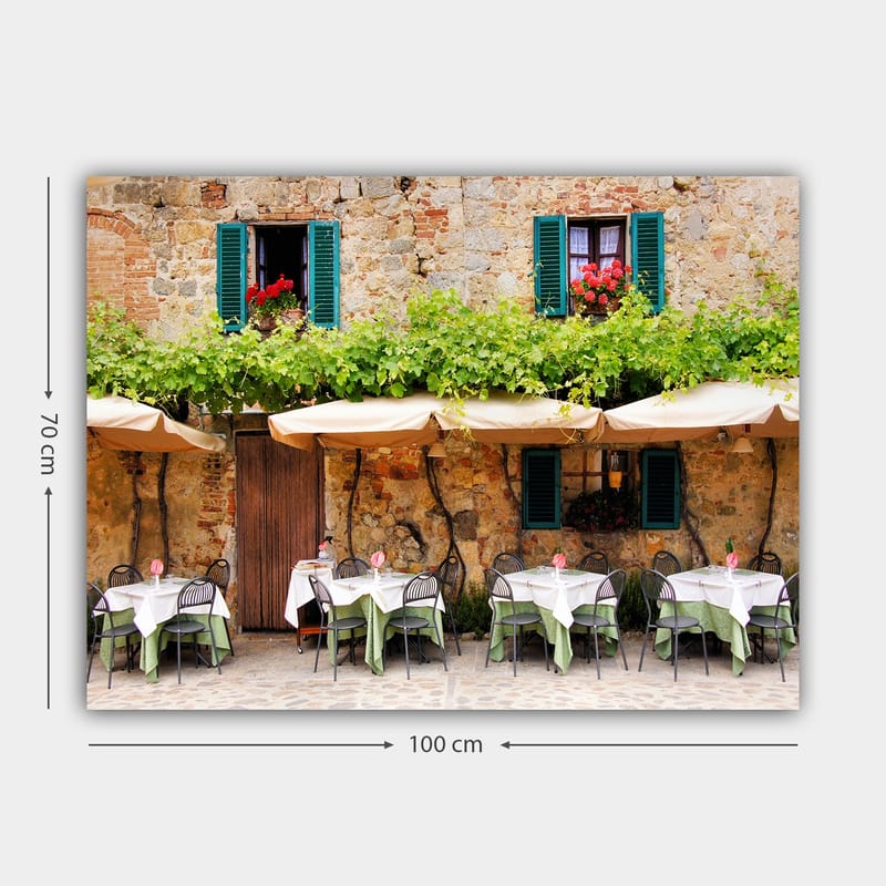 Canvastavla 70x100 cm - Charmig uteservering med vita bord och gröna dukar framför en gammal stenbyggnad med fönsterluckor i mörkgrön färg - Mörkgrön / Vit / Tegelröd - Inredning - Tavlor & posters - Canvastavla