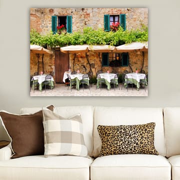 Canvastavla 70x100 cm - Charmig uteservering med vita bord och gröna dukar framför en gammal stenbyggnad med fönsterluckor i mörkgrön färg - Mörkgrön / Vit / Tegelröd - Inredning - Tavlor & posters - Canvastavla