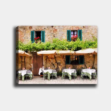 Canvastavla 70x100 cm - Charmig uteservering med vita bord och gröna dukar framför en gammal stenbyggnad med fönsterluckor i mörkgrön färg - Mörkgrön / Vit / Tegelröd - Inredning - Tavlor & posters - Canvastavla