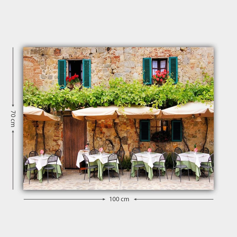 Canvastavla 70x100 cm - Charmig uteservering med vita bord och gröna dukar framför en gammal stenbyggnad med fönsterluckor i mörkgrön färg - Mörkgrön / Vit / Tegelröd - Inredning - Tavlor & posters - Canvastavla