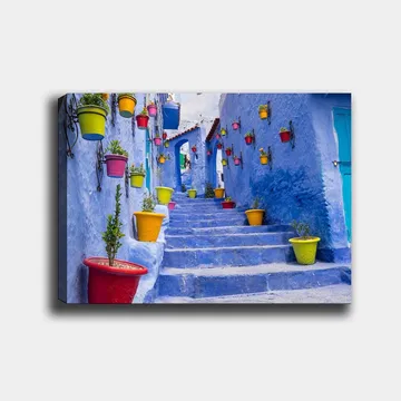 Canvastavla 70x100 cm - Färgglad trappa omgiven av blomkrukor i en pittoresk, blå stadsmiljö - Blå / Gul / Röd - Inredning - Tavlor & posters - Canvastavla
