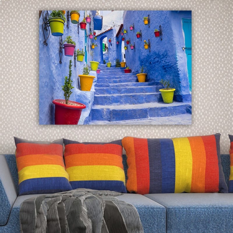 Canvastavla 70x100 cm - Färgglad trappa omgiven av blomkrukor i en pittoresk, blå stadsmiljö - Blå / Gul / Röd - Inredning - Tavlor & posters - Canvastavla