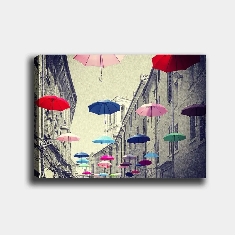 Canvastavla 70x100 cm - Färgglada paraplyer sväva över en grå stadsgata, Röd / Blå / Rosa