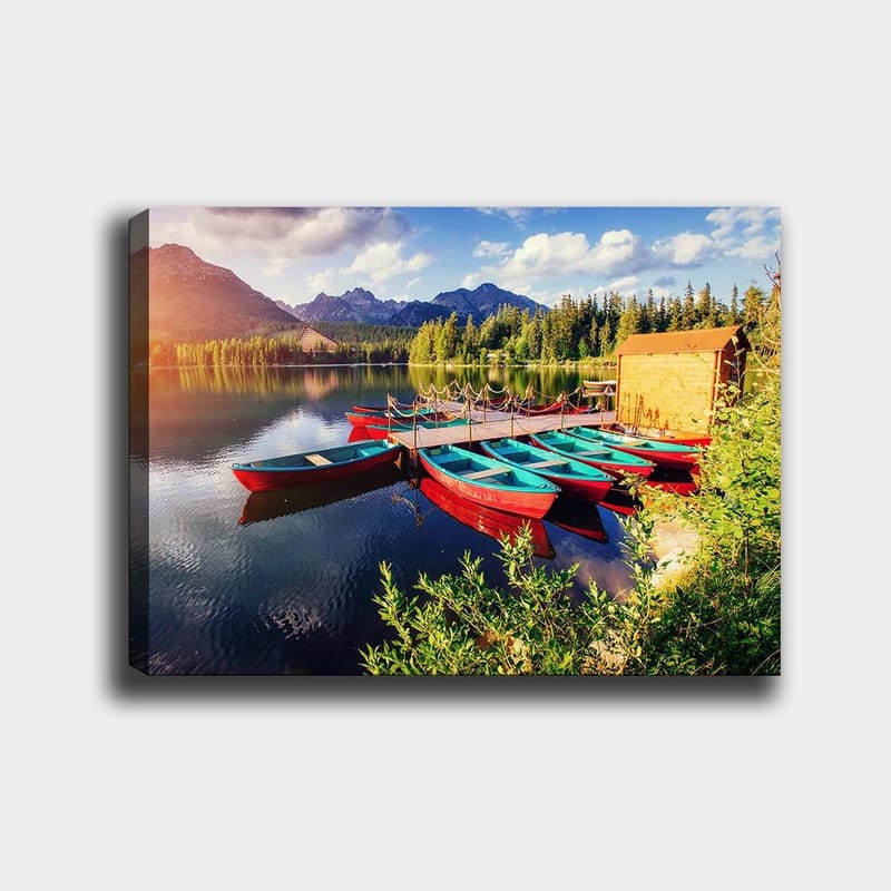 Canvastavla 70x100 cm - Flera färgglada båtar ligger vid en spegelblanka sjö omgiven av grönskande träd och berg, Röd / Turkos / Grön