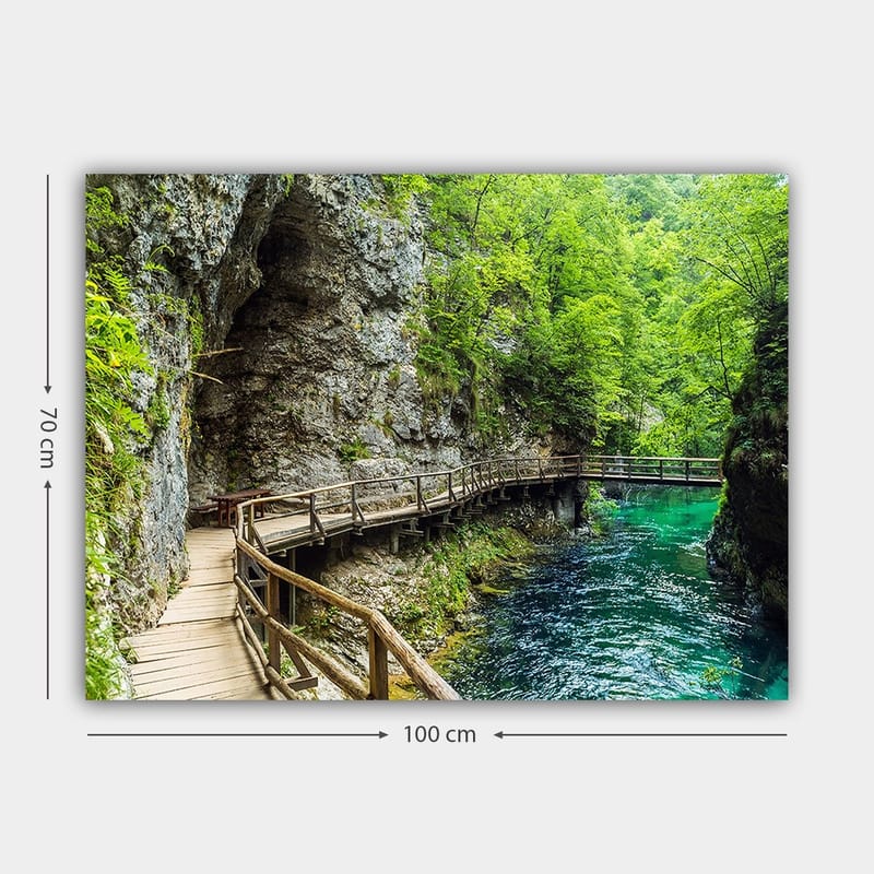 Canvastavla 70x100 cm - Naturskön vy av en träbro som slingrar sig genom en grönskande ravin vid en klar, turkos flod - Grön / Turkos / Grå - Inredning - Tavlor & posters - Canvastavla