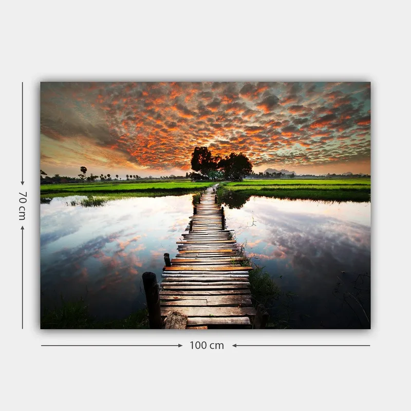 Canvastavla 70x100 cm - Träbro som sträcker sig över en spegelblanka vattenyta, omgiven av grönskande landskap och en dramatisk solnedgång - Orange / Grön / Blå - Inredning - Tavlor & posters - Canvastavla