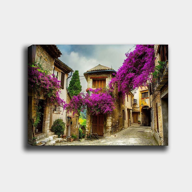 Canvastavla 70x100 cm - Pittoresk gränd omgiven av färgglada blommor i en charmig bymiljö, Lila / Grön / Beige