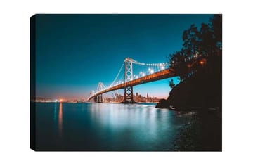 Canvastavla - Ljusbelyst bro över en stilla vattenyta med stadssilhuett i bakgrunden - Blå / Orange / Svart - Inredning - Tavlor & posters - Canvastavla